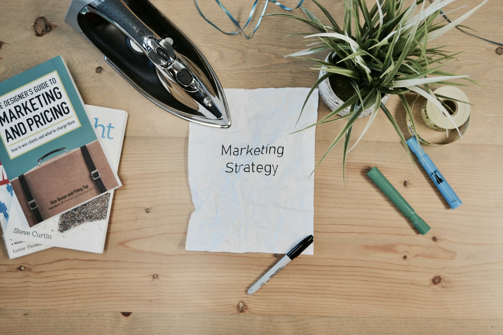 שולחן עץ עם פתק שעליו כתוב Marketing Strategy, ספרים ומגהץ